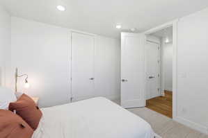 Recessed ceiling lighting illuminates a room featuring a neutral color palette, multiple white paneled doors, and a light-toned carpet leading to wood-finish flooring in the entryway