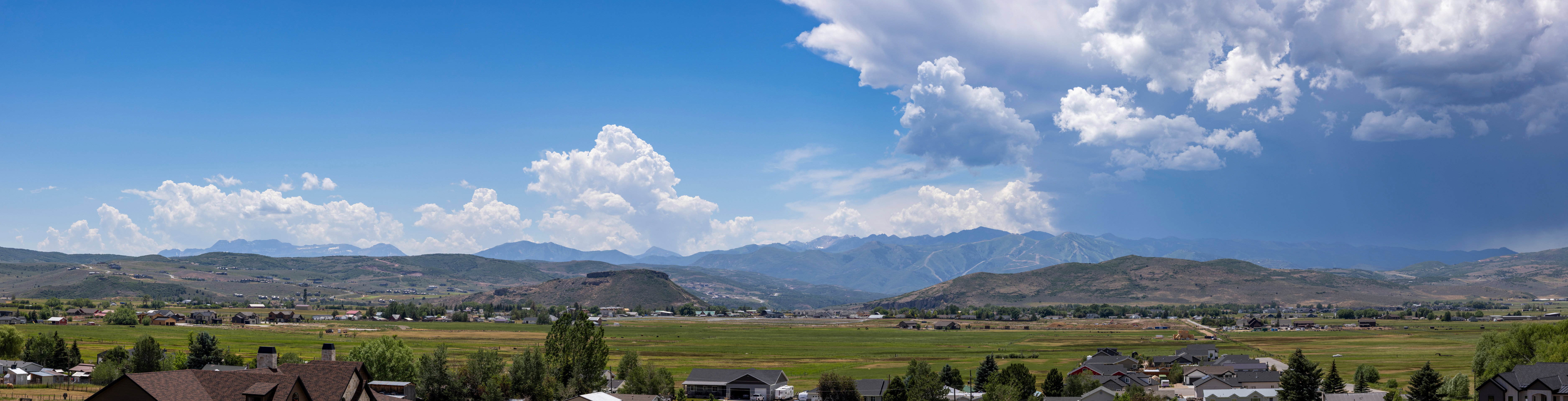 Expansive mountain range backdrop framing a valley with distant residential structures and verdant fields