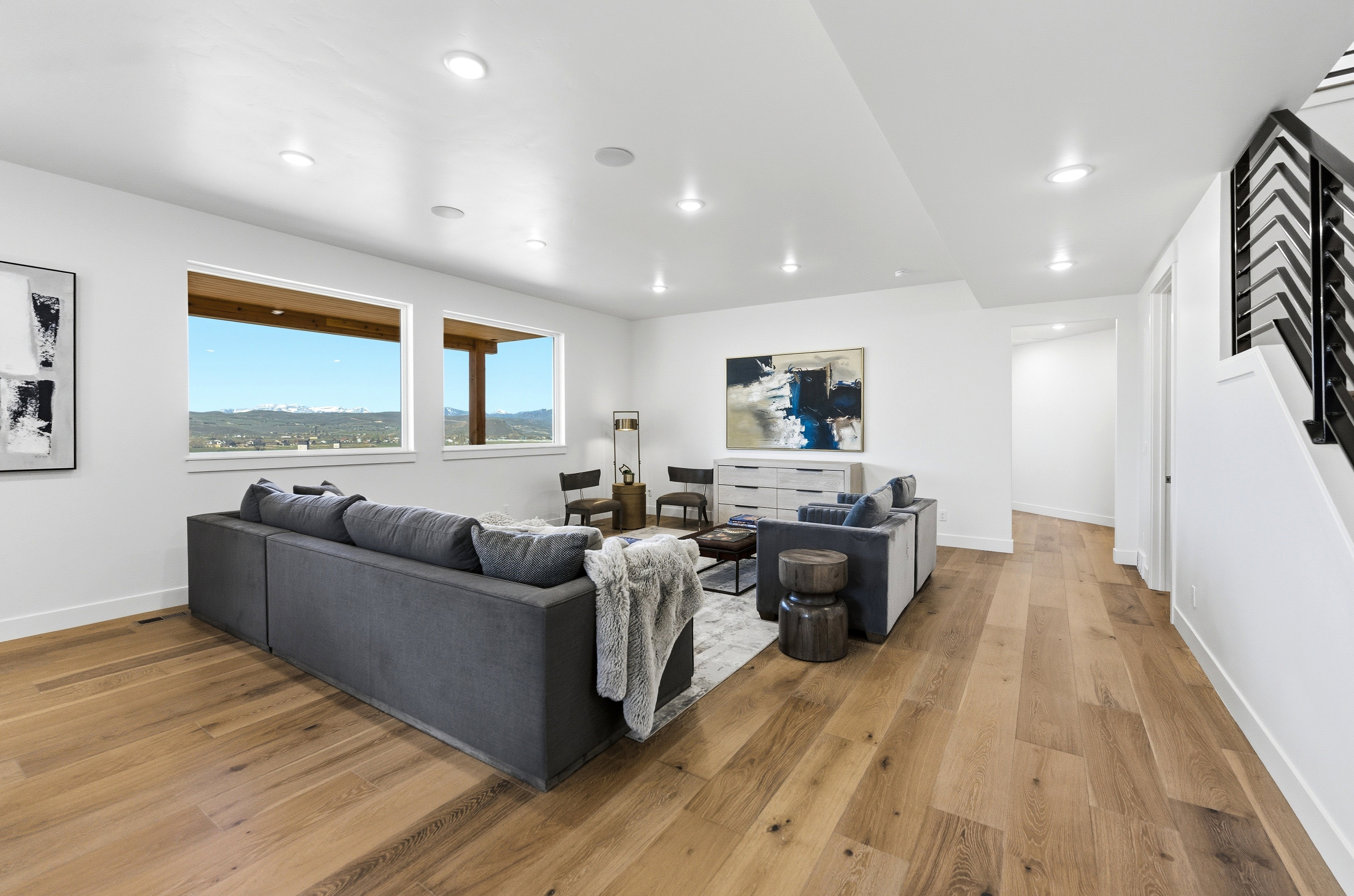 Spacious living area featuring expansive wood-finish flooring, recessed lighting, and large windows showcasing a mountain landscape