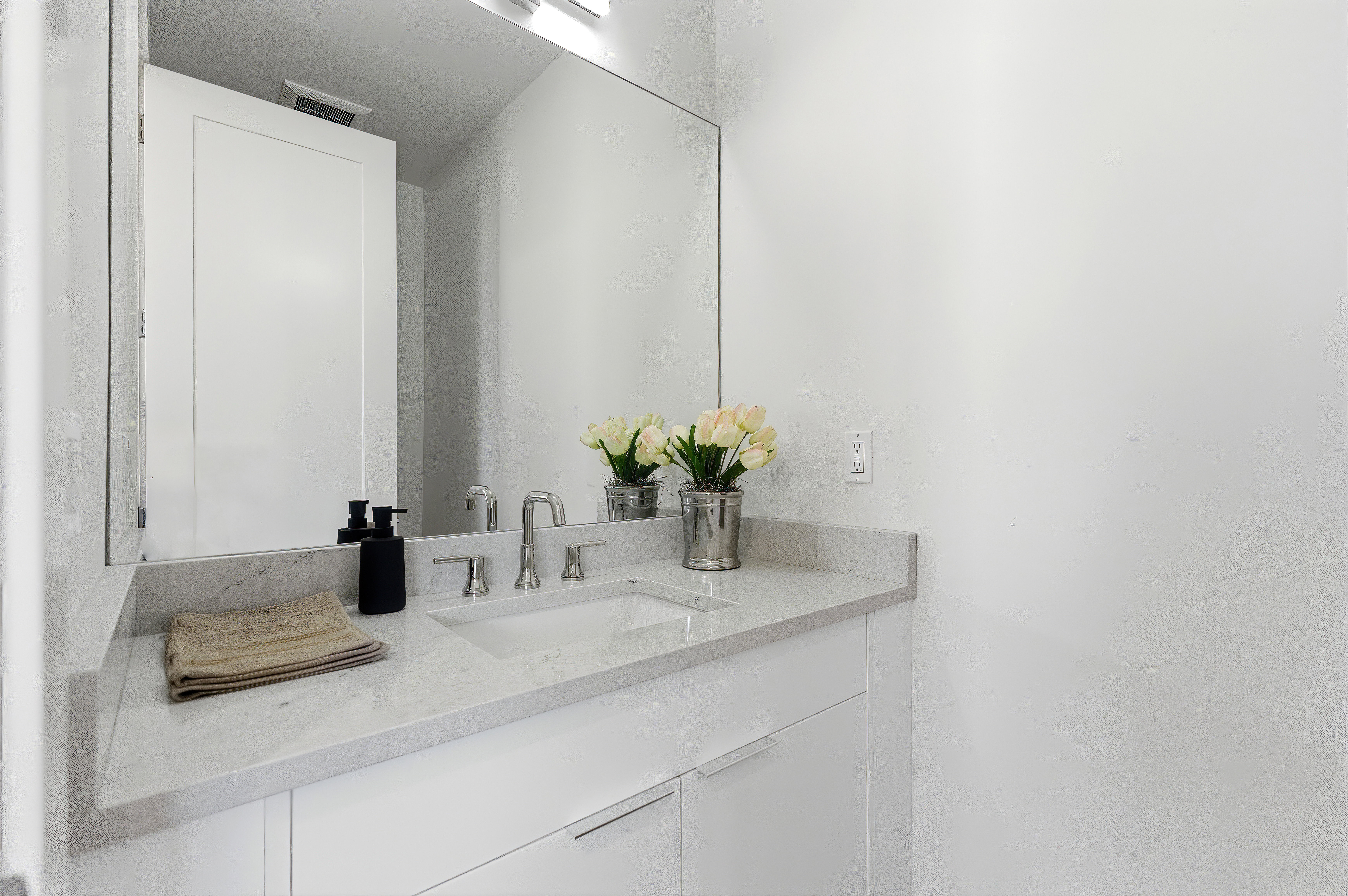 Bathroom vanity featuring a light-toned countertop, an integrated sink, and an expansive wall-mounted mirror