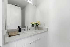 Bathroom vanity featuring a light-toned countertop, an integrated sink, and an expansive wall-mounted mirror
