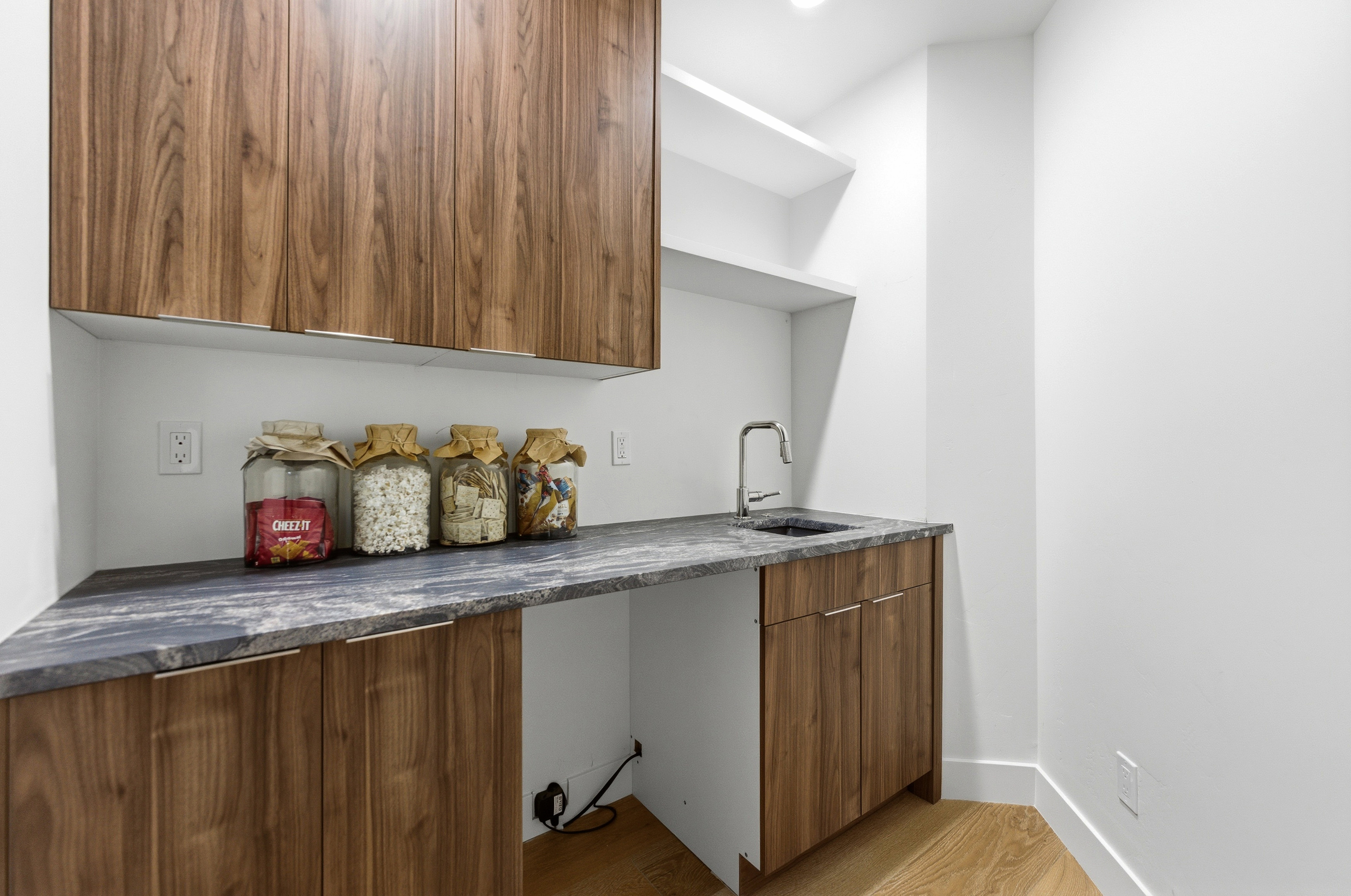 Utility space featuring wood-finish cabinetry, a stone countertop, an undermount sink with a gooseneck faucet, and light wood-finish flooring