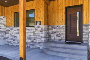 Entryway featuring a modern wood-paneled door with vertical glass insert, natural wood siding, and stone veneer accents