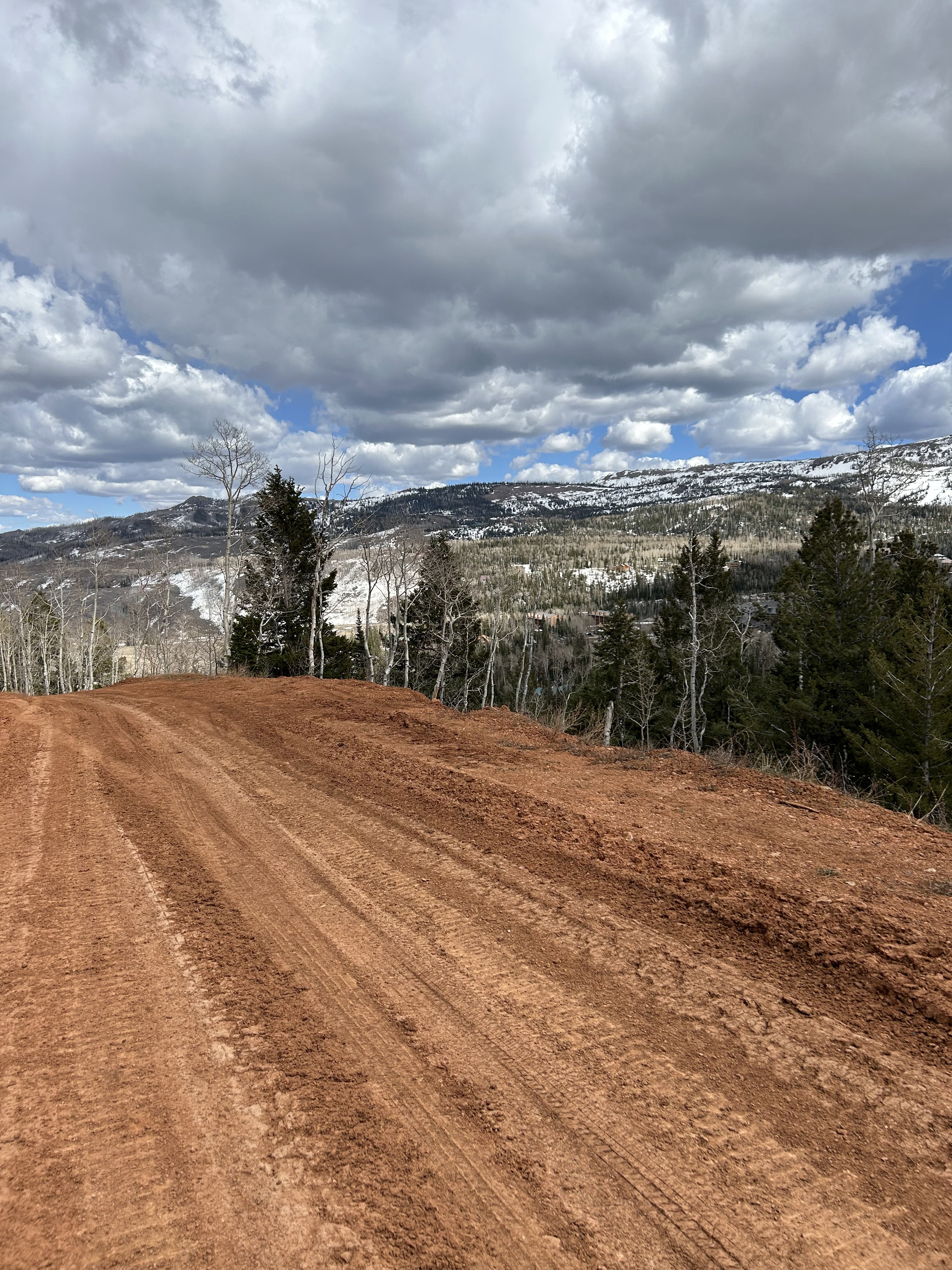 Graded lot featuring rich red soil, surrounded by evergreen and deciduous trees