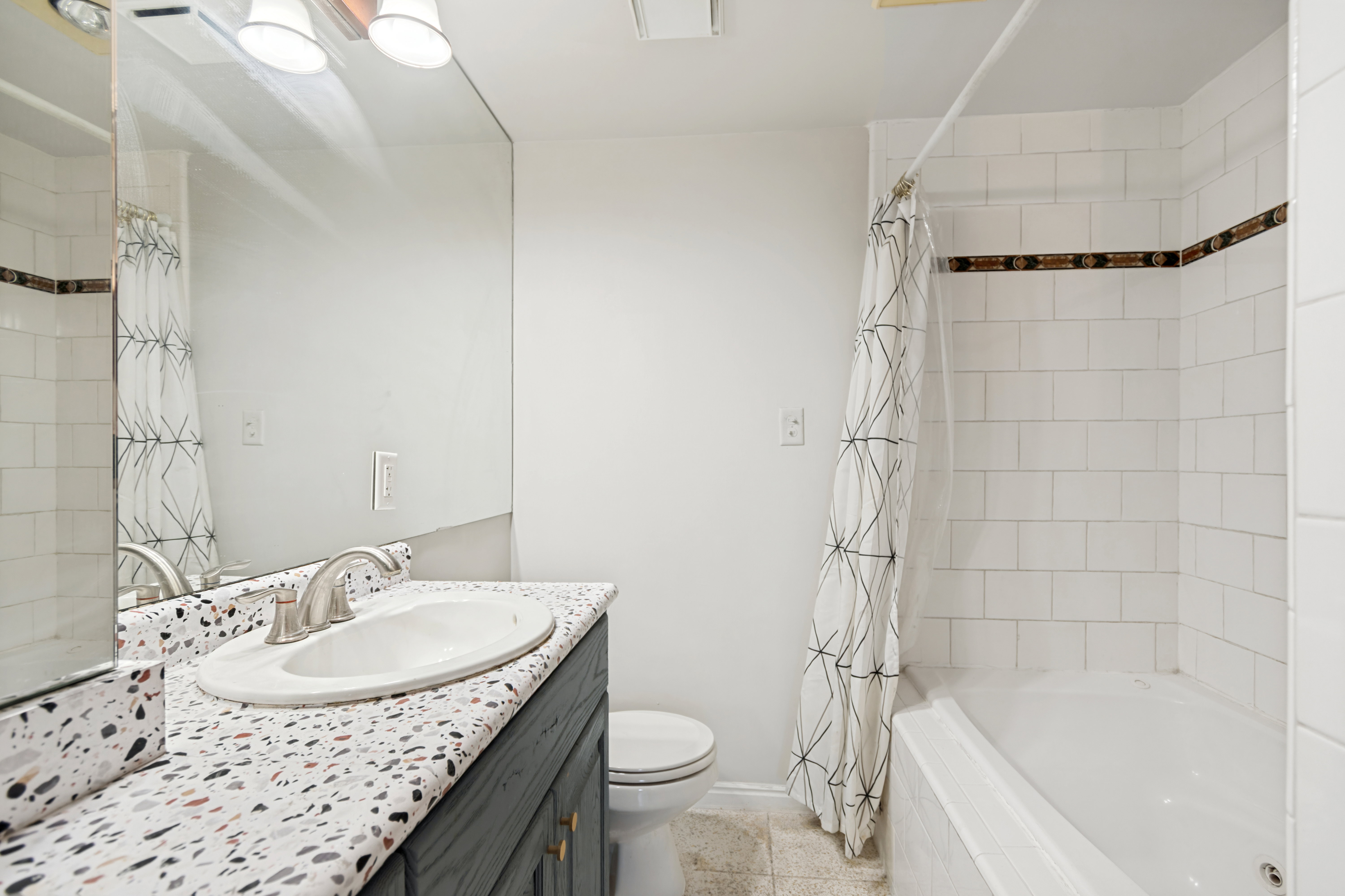 Bathroom featuring a white subway tile shower, a built-in tub, and a vanity with a terrazzo-style countertop