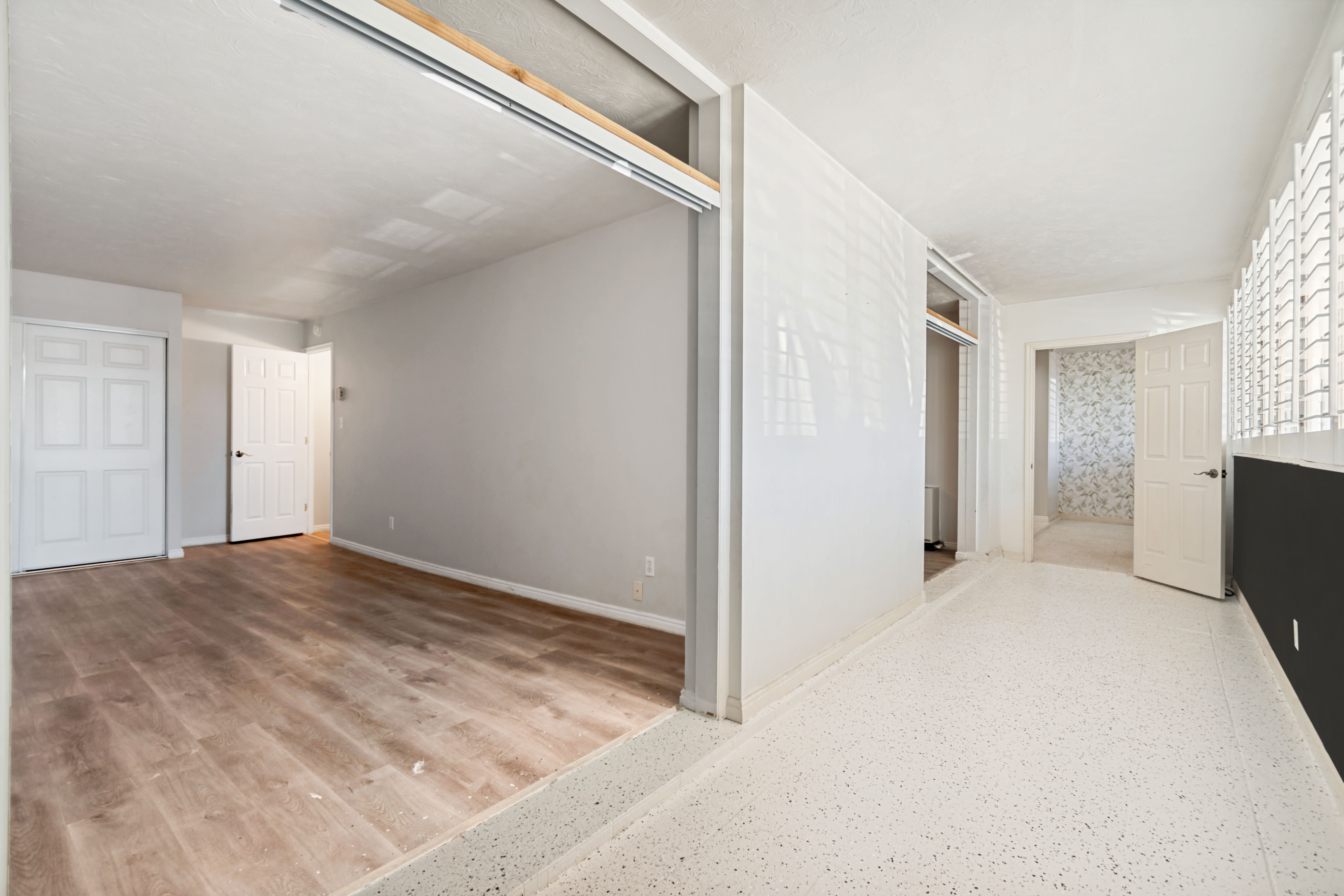 Multi-level interior featuring wood-finish flooring, white doors, and a partial wall with horizontal louvered windows