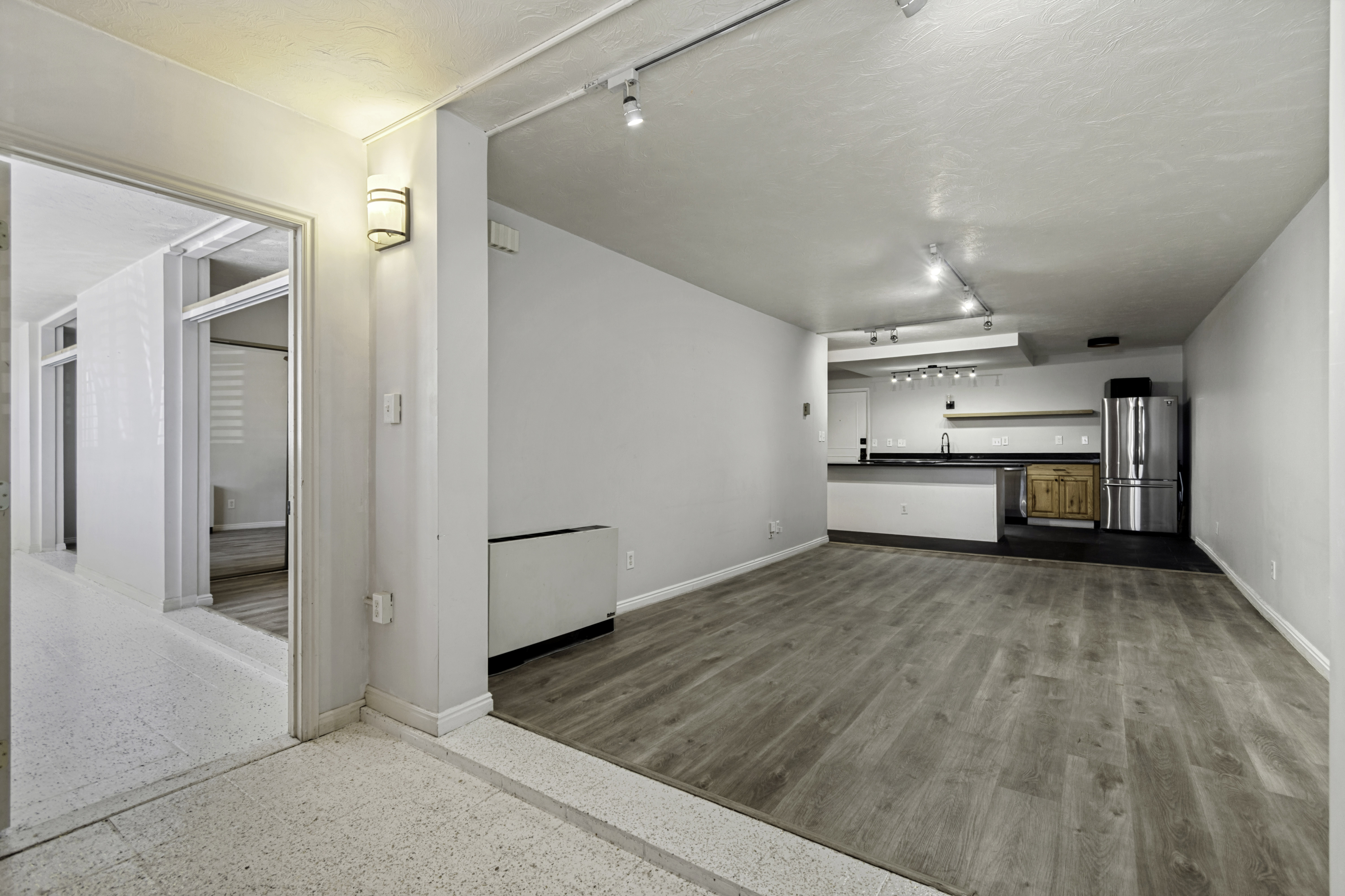 Open concept living space featuring wood-finish flooring, track lighting, and a kitchen area with a stainless steel refrigerator, dark countertops, and wood cabinetry