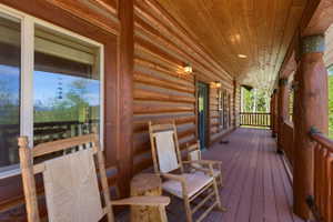Expansive covered porch featuring a log cabin exterior, wood-finish flooring, exposed wood ceiling, and built-in lighting fixtures