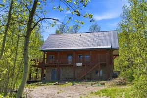 Log cabin exterior with a metal roof, featuring a stone foundation and an upper-level balcony