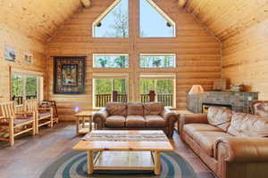 Vaulted living area featuring log wall construction, a stone-tiled fireplace, and multiple windows