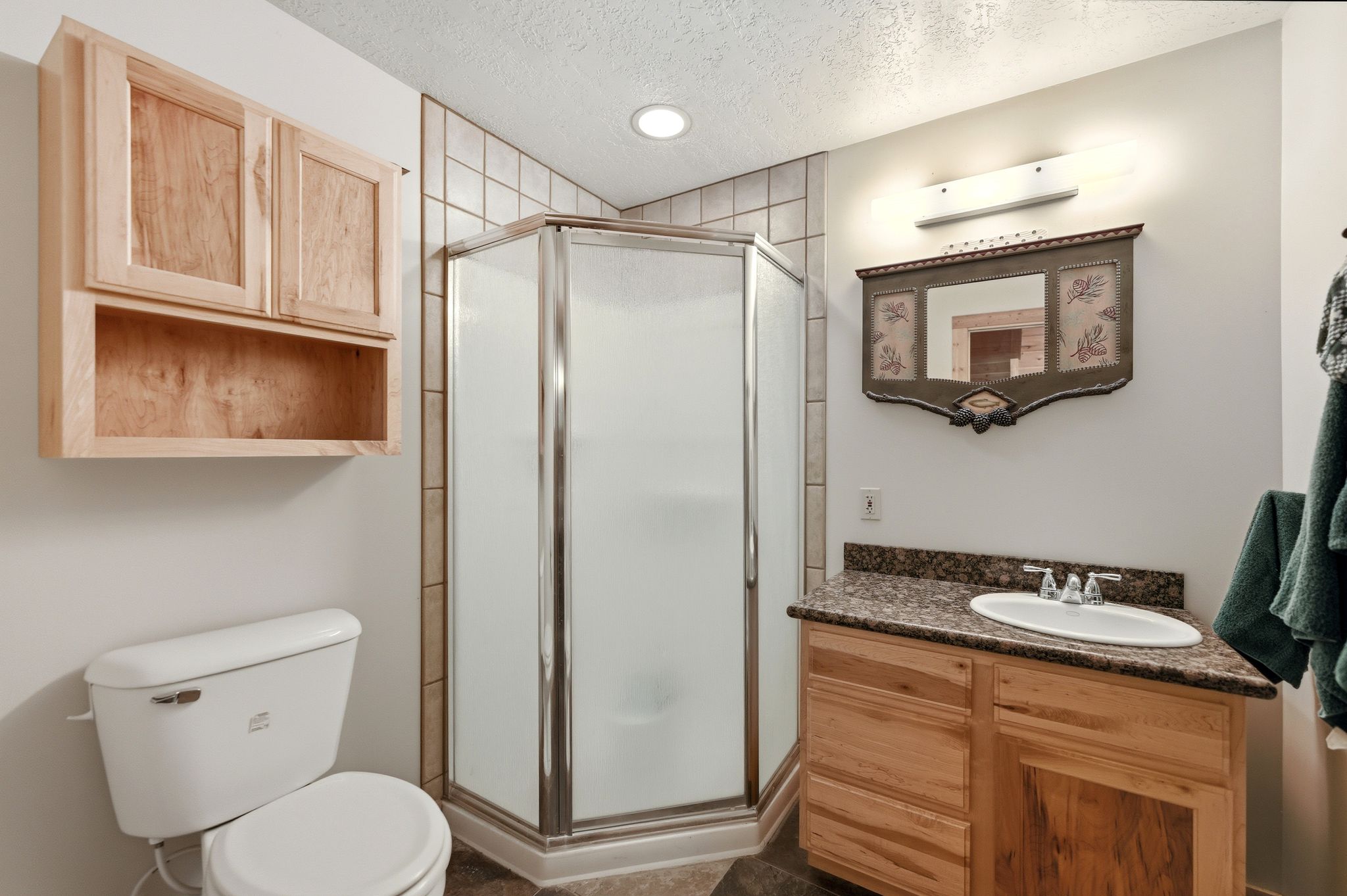 Corner shower with tiled surround, wood-finish vanity with countertop, and wood-finish wall cabinetry