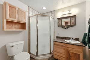 Corner shower with tiled surround, wood-finish vanity with countertop, and wood-finish wall cabinetry