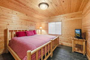 Room featuring wood-plank walls and ceiling, dark wood-finish flooring, and a single window with horizontal blinds