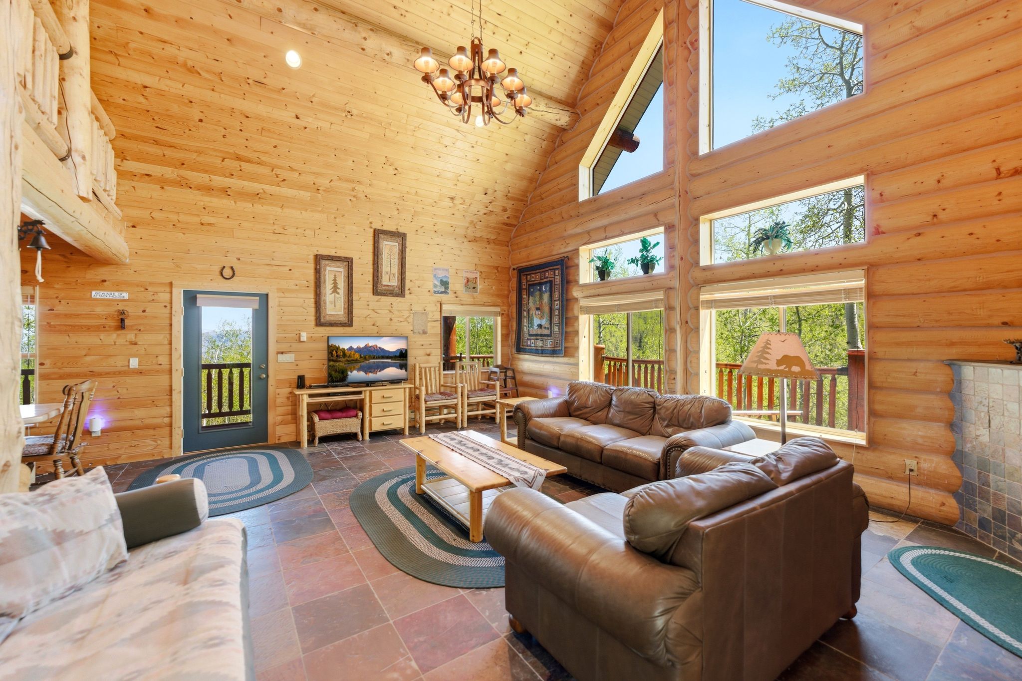 Vaulted ceiling great room featuring exposed log walls, large picture windows, and natural stone flooring