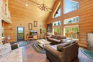 Vaulted ceiling great room featuring exposed log walls, large picture windows, and natural stone flooring