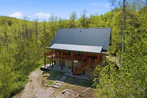 Log cabin exterior featuring a metal roof, an upper-level balcony, a ground-level patio, and natural wood stairs