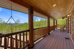 Expansive covered porch featuring a wood-finish floor, wood-paneled ceiling with recessed lighting, and log-style structural columns