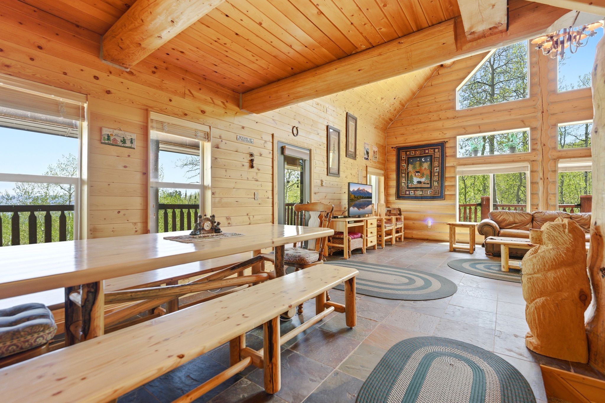 Spacious room featuring log walls, exposed log beams, a vaulted wood ceiling, multiple large windows, and dark tile flooring