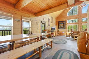 Spacious room featuring log walls, exposed log beams, a vaulted wood ceiling, multiple large windows, and dark tile flooring