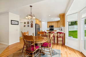 Dining area featuring a classic chandelier, wood-finish flooring, and a bay window overlooking a manicured lawn with a white picket fence