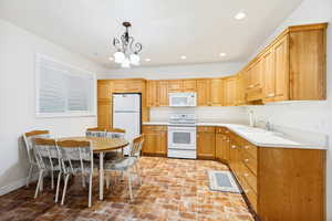 Kitchen featuring light wood cabinetry, white countertops, integrated white appliances, and a double basin sink
