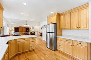 Kitchen featuring light wood cabinetry with black hardware, white countertops, stainless steel refrigerator, and wood-finish flooring