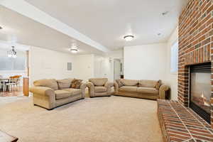 Spacious living area featuring a brick fireplace with hearth, plush carpet flooring, recessed lighting, and a window with blinds