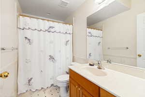 Bathroom featuring a vanity with wood-finish cabinetry, a single basin sink, a large wall mirror, and a white toilet