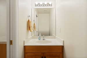 Powder room featuring a single vanity with wood-finish cabinetry, a white countertop with an integrated sink, and an overhead four-bulb light fixture