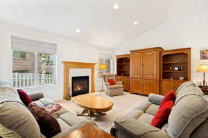Spacious living area featuring a fireplace with a light wood mantel, vaulted ceilings, recessed lighting, and large windows
