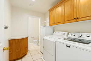 Utility room featuring light wood-finish cabinetry, a corner countertop, and neutral tile flooring