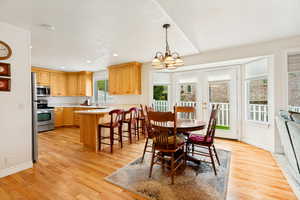 Kitchen and dining area featuring wood-finish flooring, light wood cabinetry, stainless steel appliances, a breakfast bar, and multiple windows with white trim