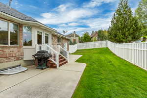 Expansive fenced backyard featuring a concrete patio, wood steps with white railings, and a wide grassy area