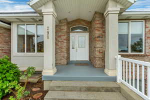 Brick exterior featuring a covered porch, white entry door with decorative glass, two large windows, concrete steps, and a white railing