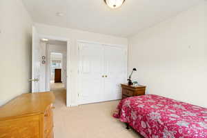 Neutral-toned carpeted room featuring a double-door closet with gold-finish hardware, a white paneled entry door, and light cream wall finishes