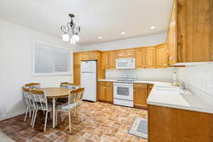 Kitchen area featuring abundant wood-finish cabinetry, a white double-basin sink, and white appliances