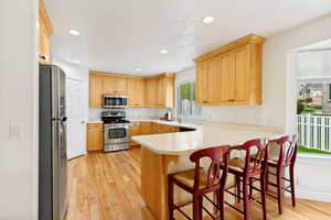Spacious kitchen featuring wood-finish flooring, light-toned cabinetry with crown molding, stainless steel appliances, a white countertop, and recessed lighting