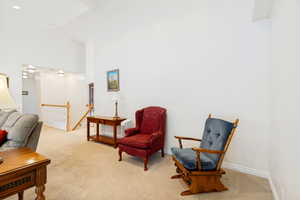 Vaulted ceilings enhance this carpeted living area, featuring a staircase with white spindles and a wood handrail