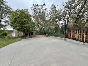 Spacious concrete patio featuring a basketball hoop, surrounded by mature trees and a wooden privacy fence
