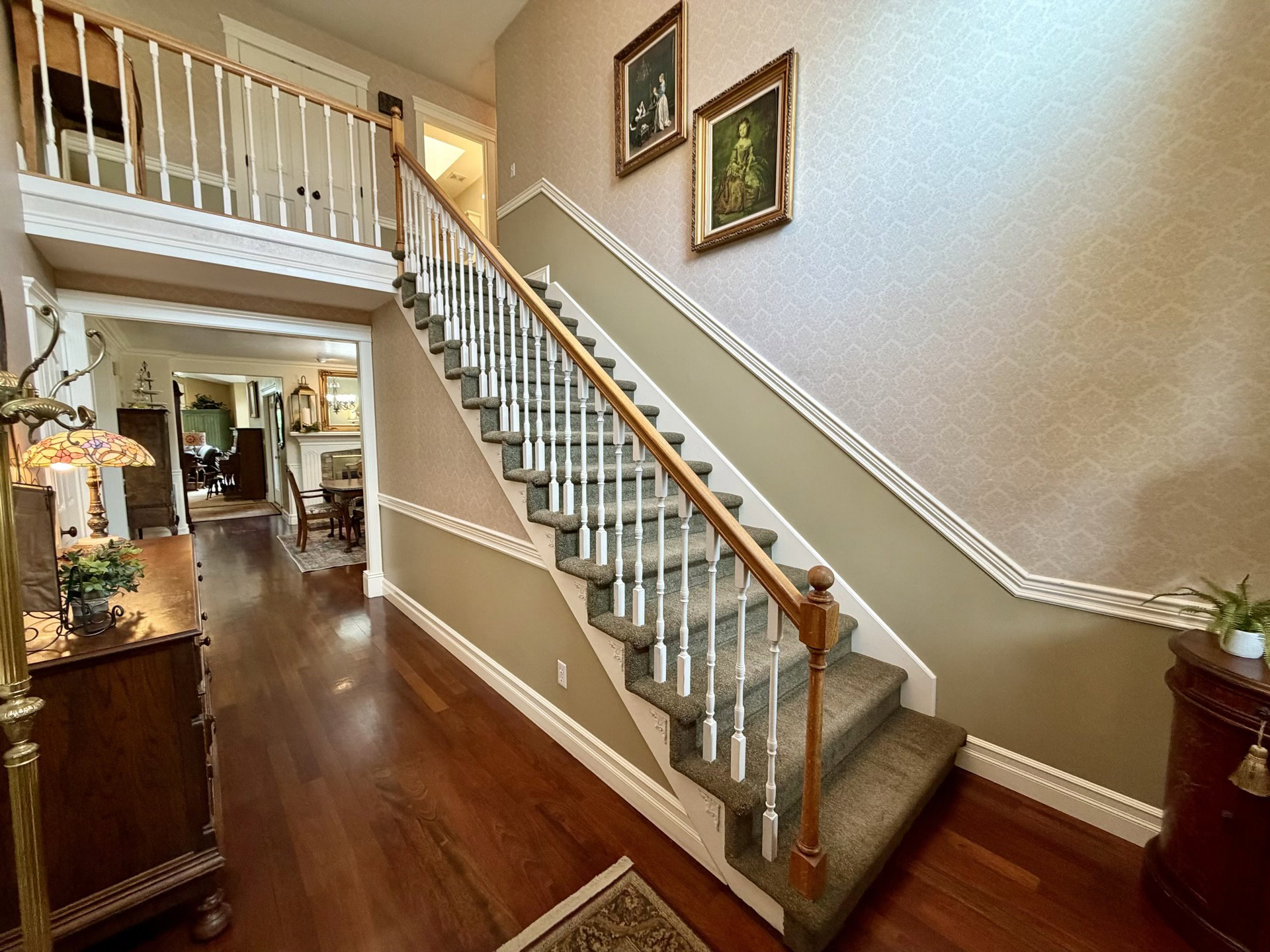 Two-story foyer featuring dark wood-finish flooring, a grand staircase with carpeted treads, white balusters, and a natural wood handrail