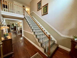 Two-story foyer featuring dark wood-finish flooring, a grand staircase with carpeted treads, white balusters, and a natural wood handrail