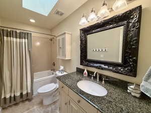 Bathroom featuring a skylight, a single vanity with a speckled countertop, an ornate framed mirror, and a built-in bathtub with shower