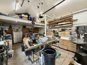 Workshop space featuring a vaulted ceiling, integrated overhead storage, wall-mounted lumber racks, and extensive built-in cabinetry with wood-finish drawers
