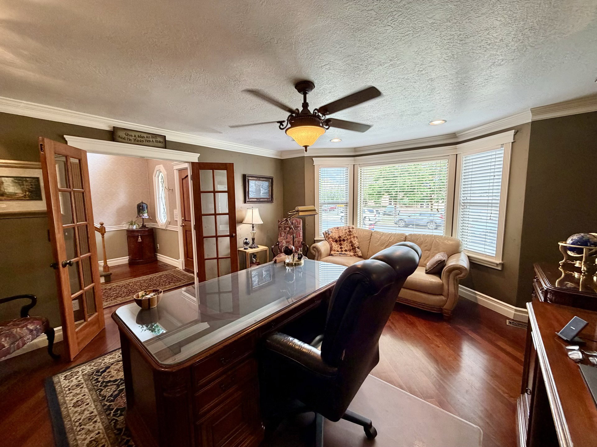 Dedicated office space featuring rich wood-finish flooring, a multi-pane bay window with blinds, and crown molding