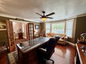 Dedicated office space featuring rich wood-finish flooring, a multi-pane bay window with blinds, and crown molding