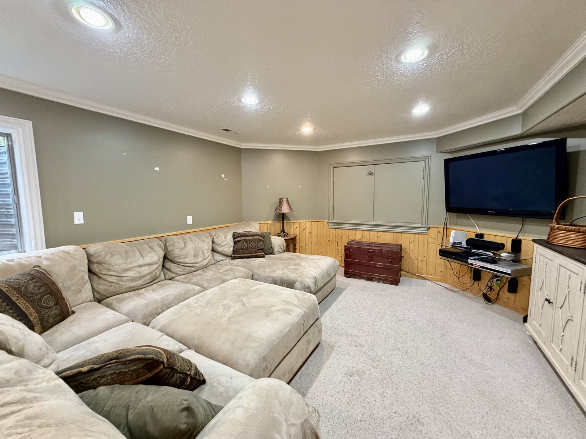 Recessed lighting illuminates this carpeted room featuring painted walls with wood paneling and crown molding