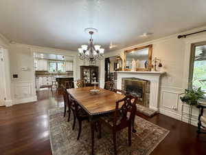 Formal dining space with rich wood-finish flooring, a traditional fireplace with a brick surround, and white wainscoting