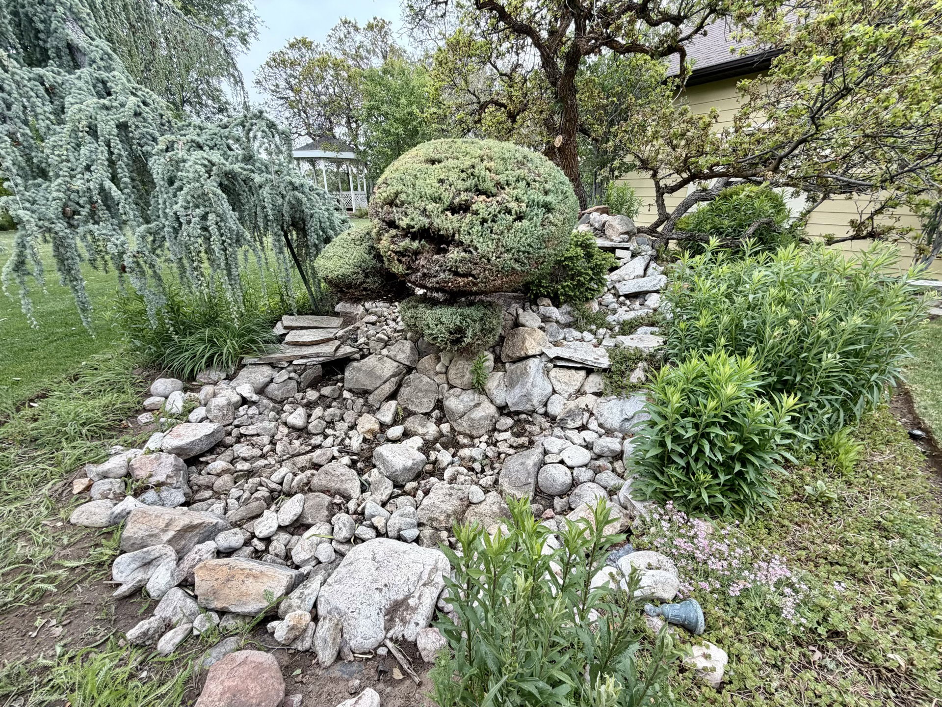 Garden landscaping featuring a dry creek bed, varied rock formations, and mature plantings