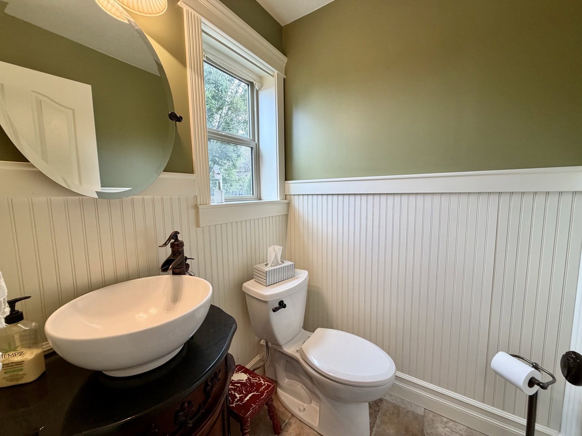 Bathroom featuring a vessel sink atop a dark wood-finish vanity, beadboard wainscoting, and a window with white trim