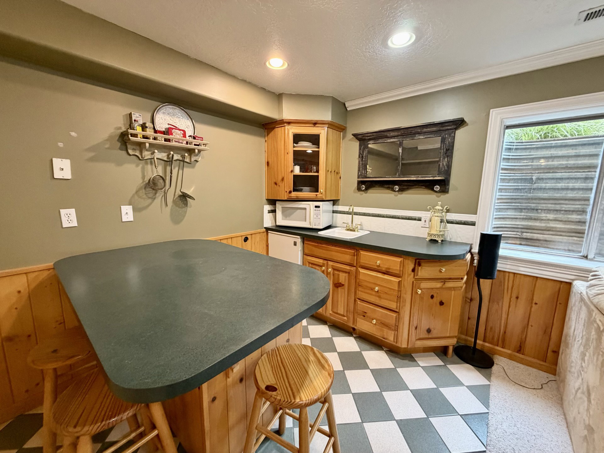 Functional kitchenette featuring wood-finish cabinetry, a sink with brass-finish faucet, and a black and white checkerboard floor